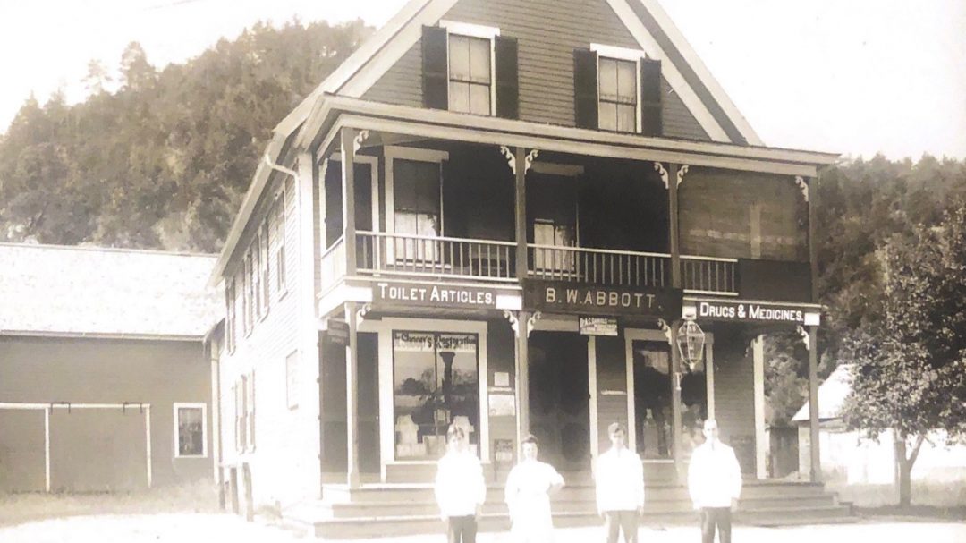 A black and white picture of the store many years ago. Four people standing in front of it.
