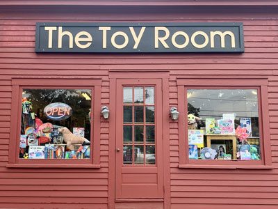 The front door of Chapman's Toy Room. Toys can be see through the windows. There is a large sign above the door in gold that says Chapman's Toy Room