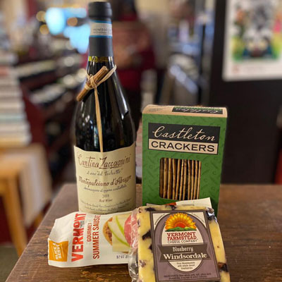 A bottle of wine on a table next to a box of crackers and a package of cheese.